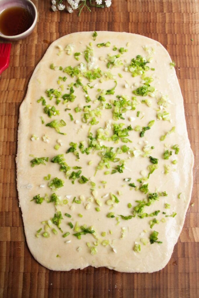 Scallions sprinkled over rolled out dough on a wooden board.