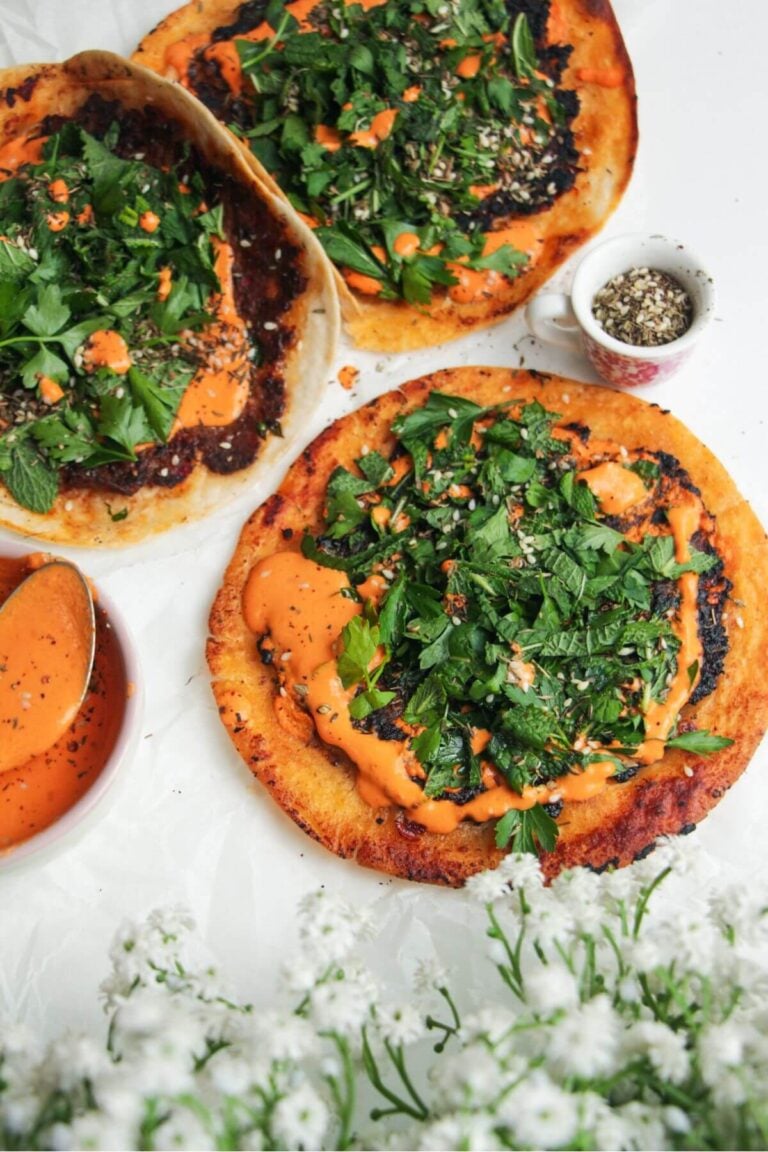 Smash lahmacun taco with red pepper sauce and herby salad on top.