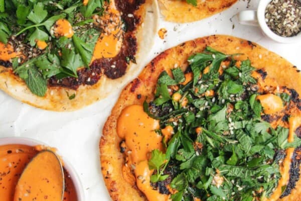 Smash lahmacun taco with red pepper sauce and herby salad on top.