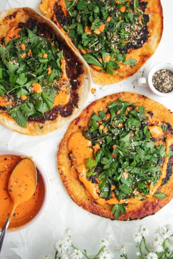 Smash lahmacun taco with red pepper sauce and herby salad on top.