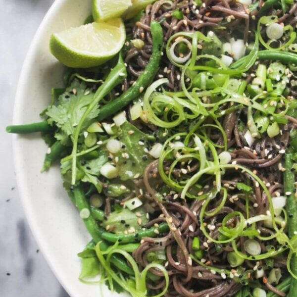 Cold Asian soba noodle salad with lots of green vegetables in a large serving platter, with jug of dressing on the side.