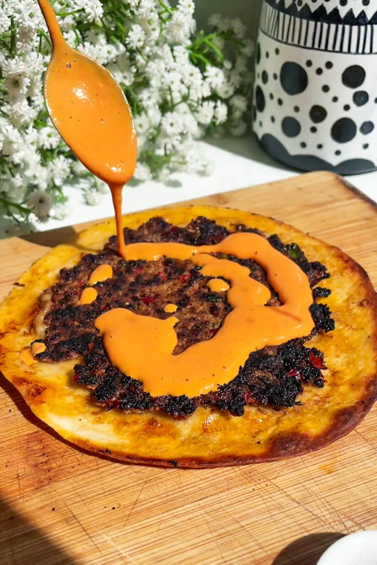 Drizzling red pepper sauce on top of a smash lahmacun taco.