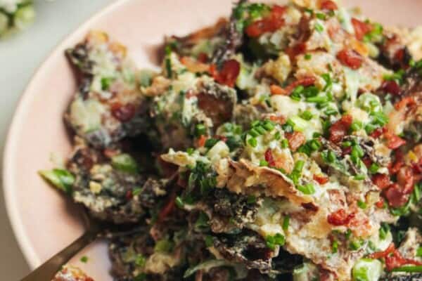 Smashed potato salad in a pink bowl with chives scattered on top.