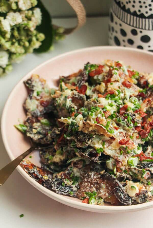 Smashed potato salad in a pink bowl with chives scattered on top.