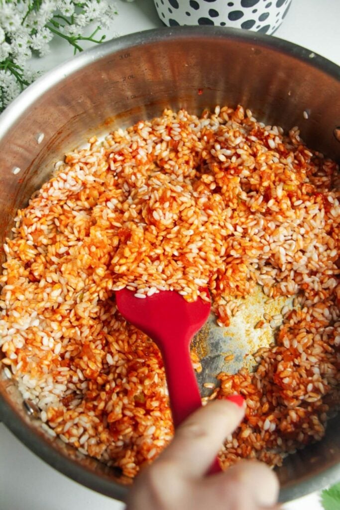 Rice added to a large pan, being stirred with a spatula.