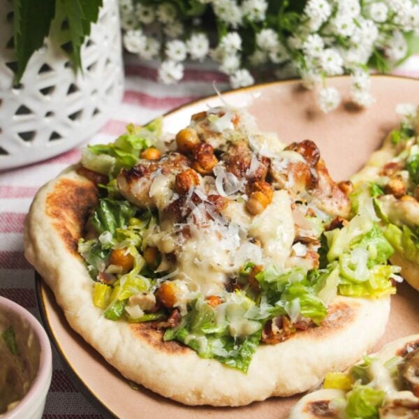 Flatbread on a plate topped with Caesar salad, charred chicken pieces and creamy Caesar dressing.