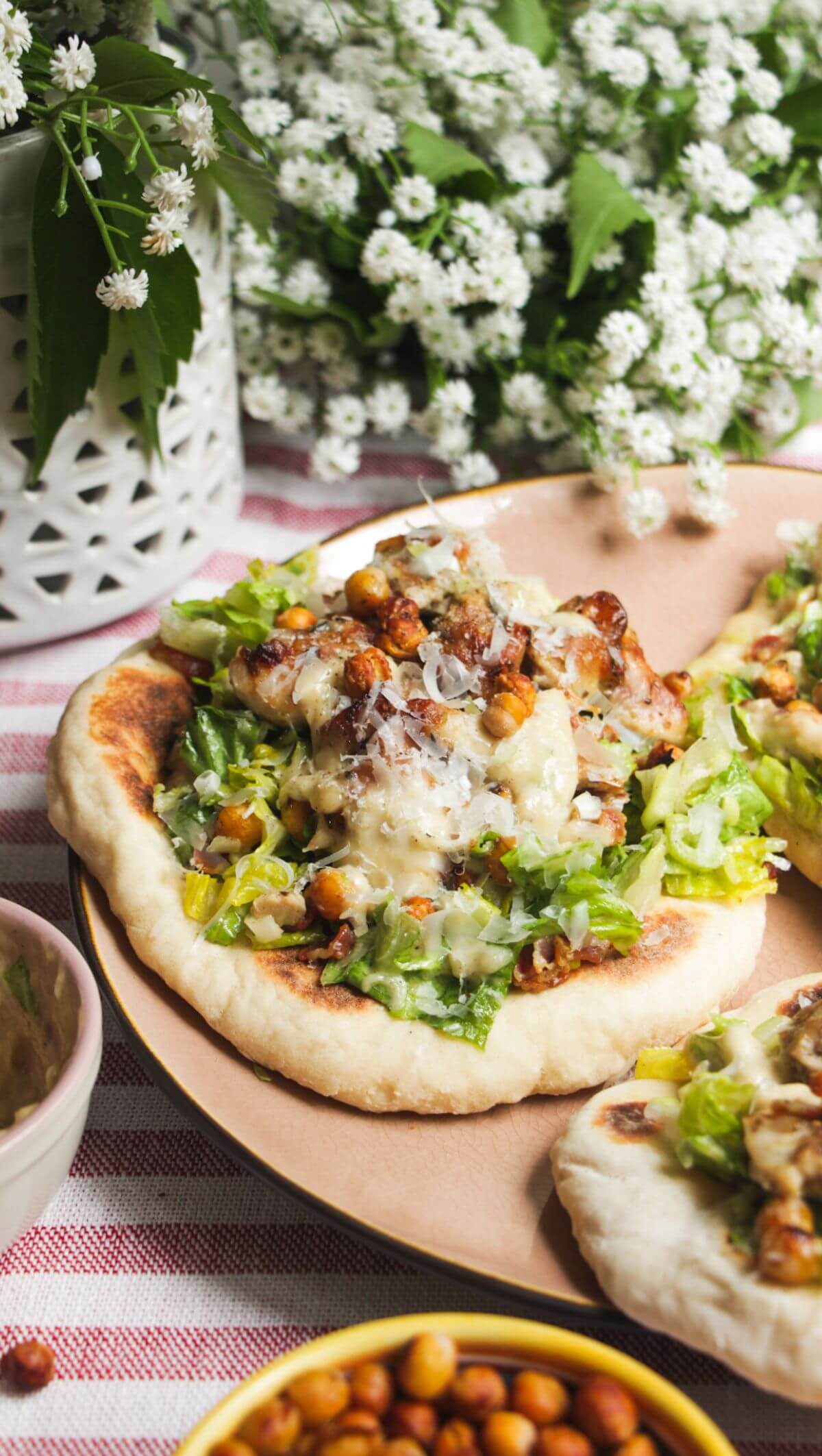Flatbread on a plate topped with Caesar salad, charred chicken pieces and creamy Caesar dressing.