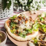 Flatbread on a plate topped with Caesar salad, charred chicken pieces and creamy Caesar dressing.
