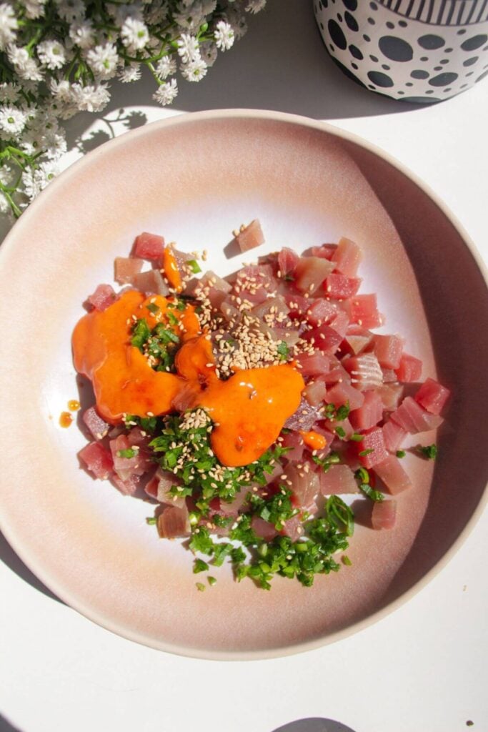 Diced tuna in a pink bowl with spicy mayo, scallions and sesame seeds.