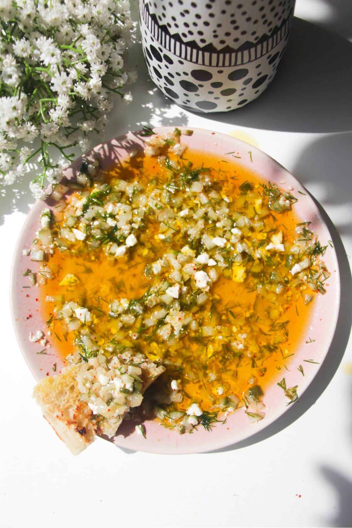 Dill pickle dipping oil on a pink plate with a piece of focaccia on the side.