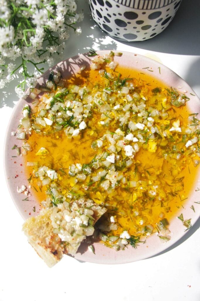 Dill pickle dipping oil on a pink plate with a piece of focaccia on the side.