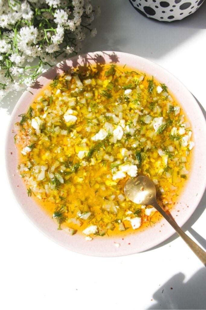 Dill pickle dipping oil mixed in a small pink plate with a gold spoon on the side.