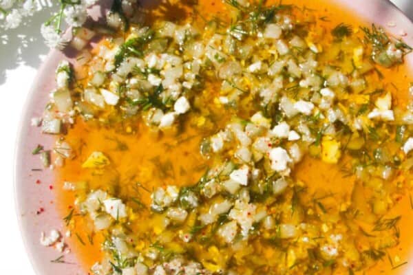 Dill pickle dipping oil on a pink plate with a piece of focaccia on the side.