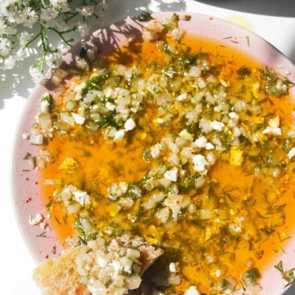 Dill pickle dipping oil on a pink plate with a piece of focaccia on the side.