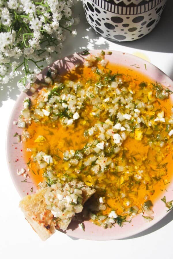 Dill pickle dipping oil on a pink plate with a piece of focaccia on the side.