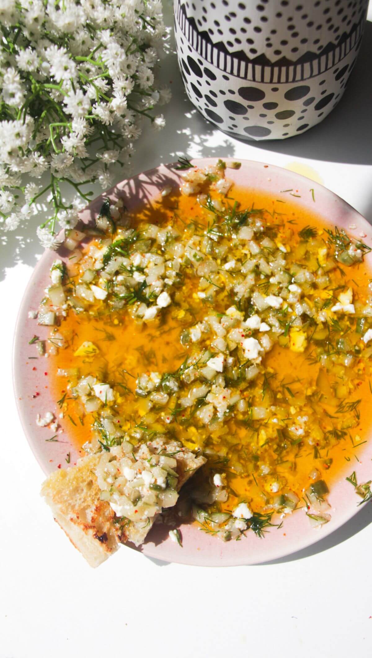 Dill pickle dipping oil on a pink plate with a piece of focaccia on the side.