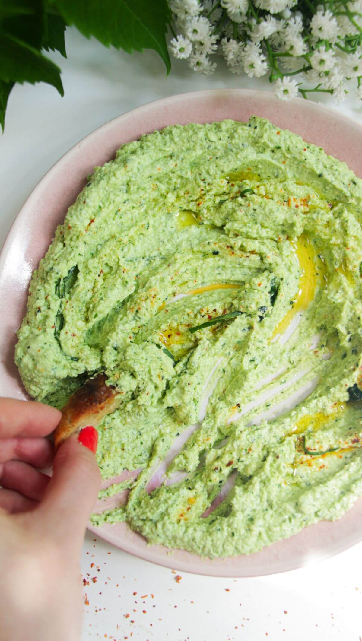 Whipped feta pesto dip on a pink plate with a small piece of bread on thes side.