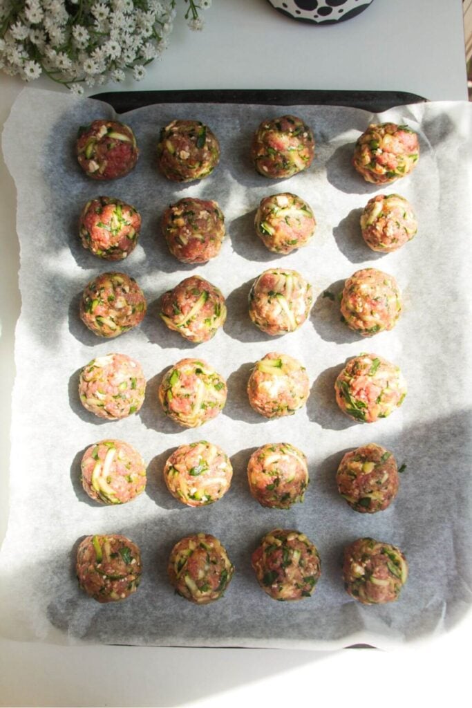Rolled meatballs on a lined oven tray.