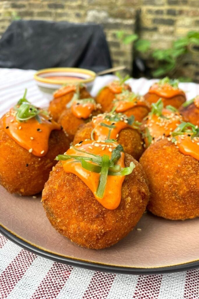 Crispy arancini balls on a pink plate and topped with spicy aioli on top.