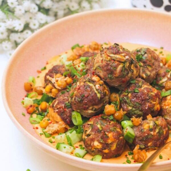Meatballs piled on top of smoky red pepper sauce with flowers in the background.