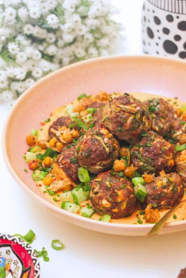 Meatballs piled on top of smoky red pepper sauce with flowers in the background.
