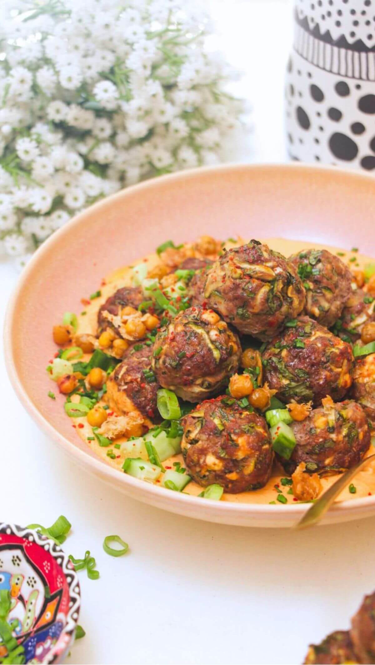 Meatballs piled on top of smoky red pepper sauce with flowers in the background.