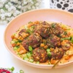 Meatballs piled on top of smoky red pepper sauce with flowers in the background.