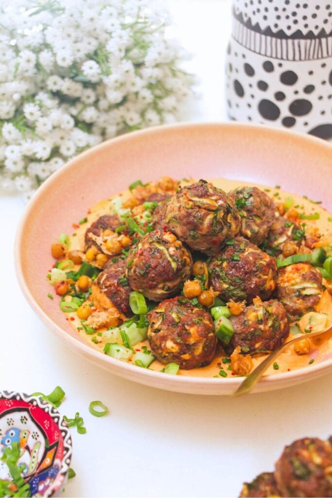 Meatballs piled on top of smoky red pepper sauce with flowers in the background.