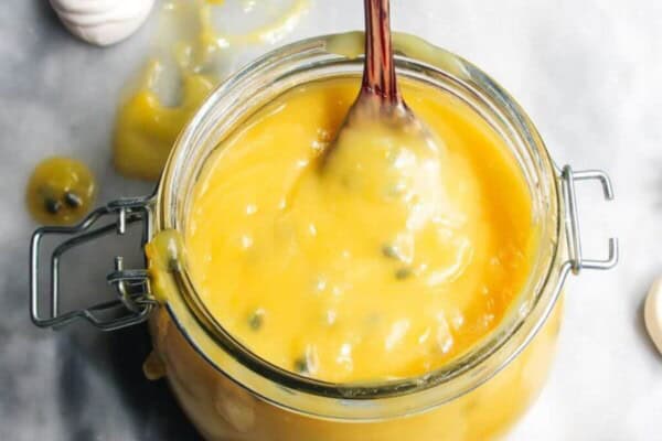 Lemon and passionfruit in a glass jar with a spoon in it.