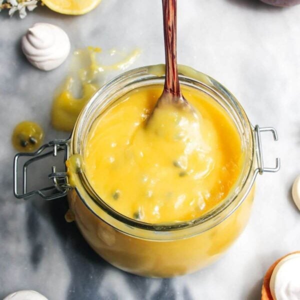 Lemon and passionfruit in a glass jar with a spoon in it.