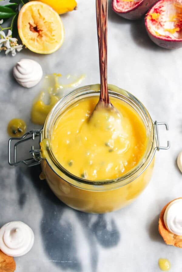 Lemon and passionfruit in a glass jar with a spoon in it.