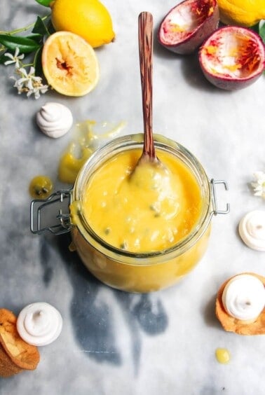 Lemon and passionfruit in a glass jar with a spoon in it.