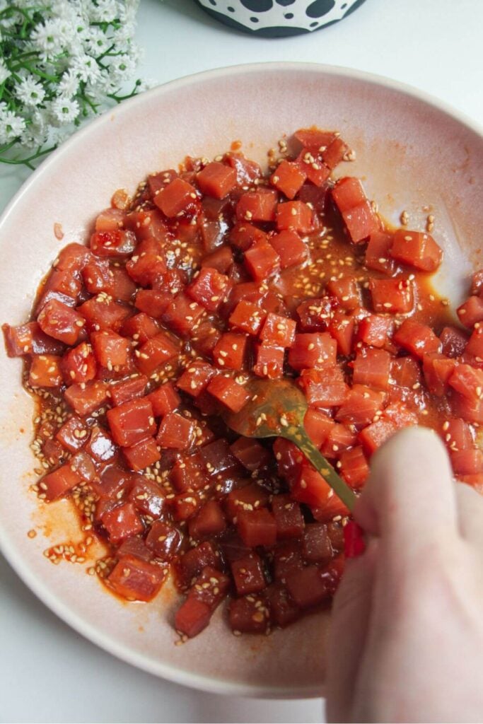 Mixing diced tuna through marinade in a bowl.