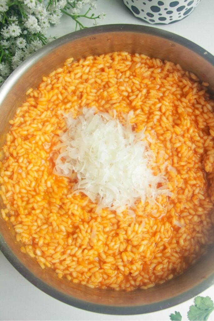 Grated parmesan on top of cooked gochujang risotto in a pan.