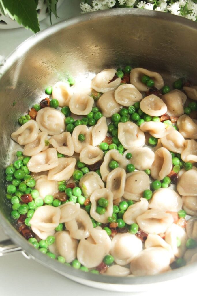Pasta tossed through peas and pancetta in a pan.