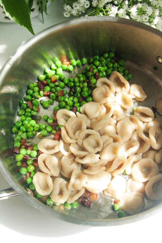 Cooked pasta added to a pan with peas and pancetta.