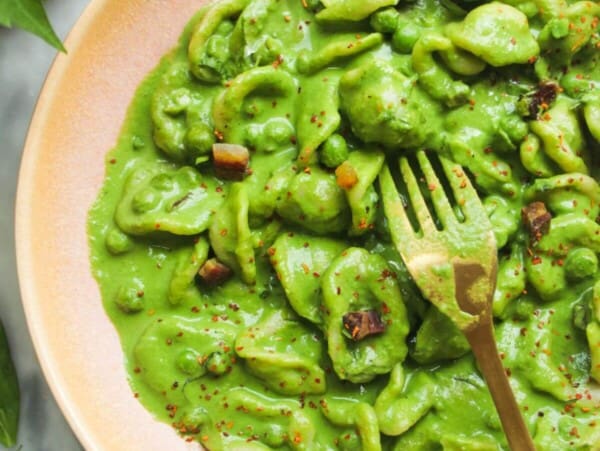 Pea pancetta carbonara in a pink bowl with a gold fork.