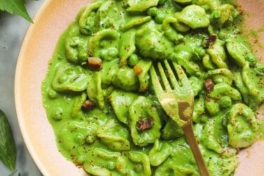Pea pancetta carbonara in a pink bowl with a gold fork.
