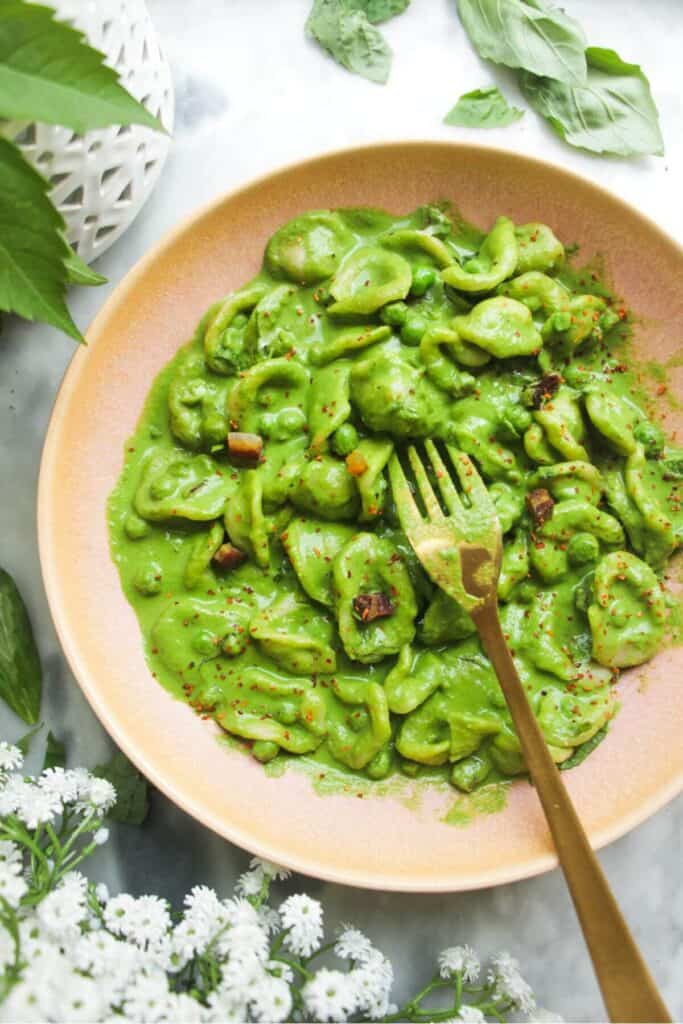 Pea pancetta carbonara in a pink bowl with a gold fork.