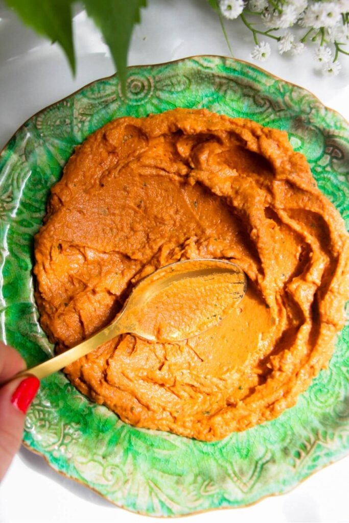 Smoothing sundried tomato basil hummus onto a green plate with a spoon.