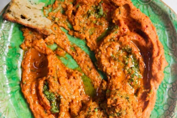 Sundried tomato basil hummus on a green plate with a piece of bread on the side.
