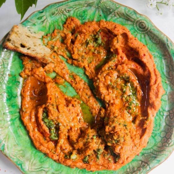 Sundried tomato basil hummus on a green plate with a piece of bread on the side.