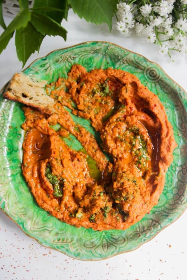 Sundried tomato basil hummus on a green plate with a piece of bread on the side.