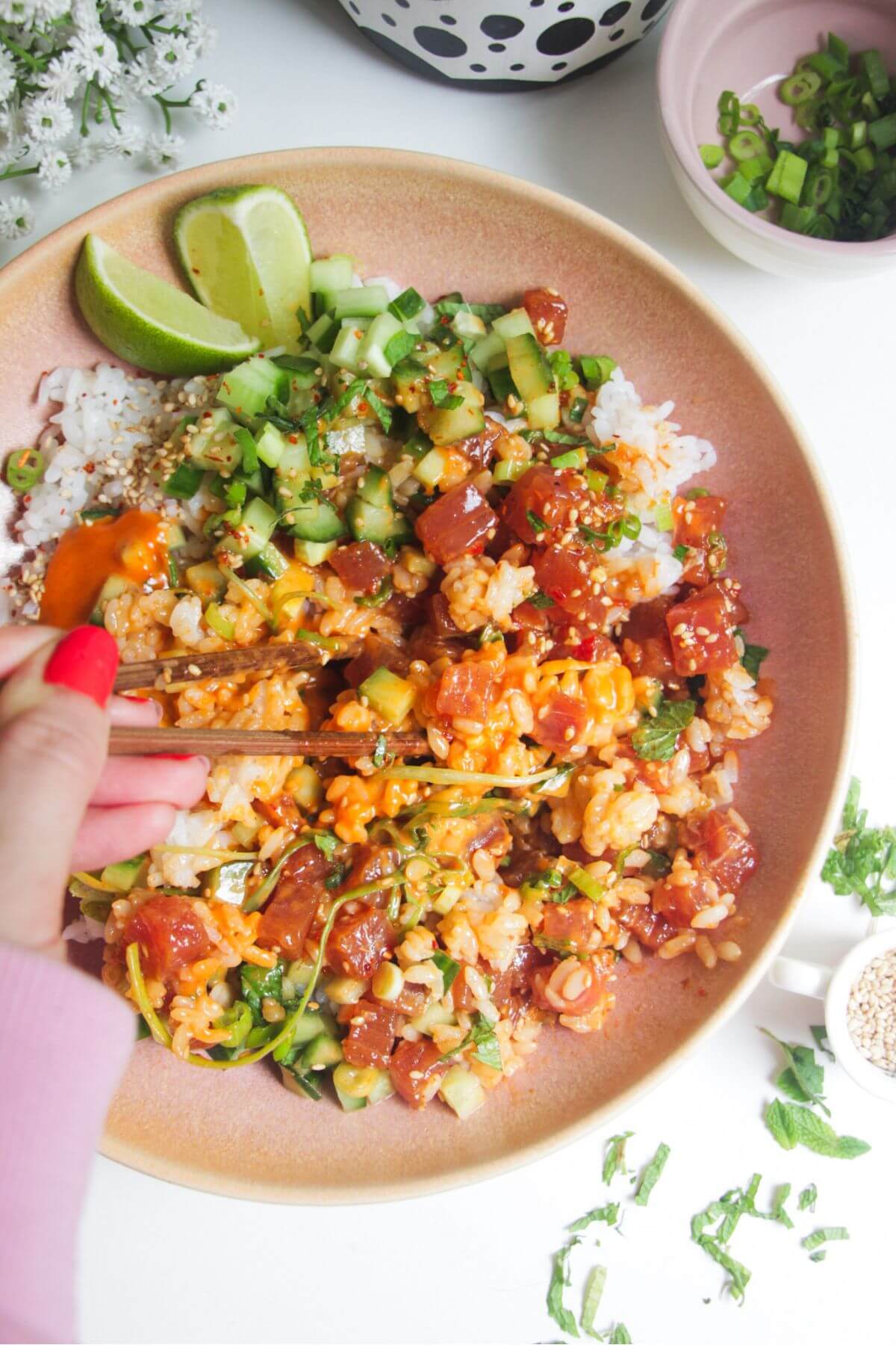 Hands holding chopsticks, picking up tuna in tuna poke bowl.