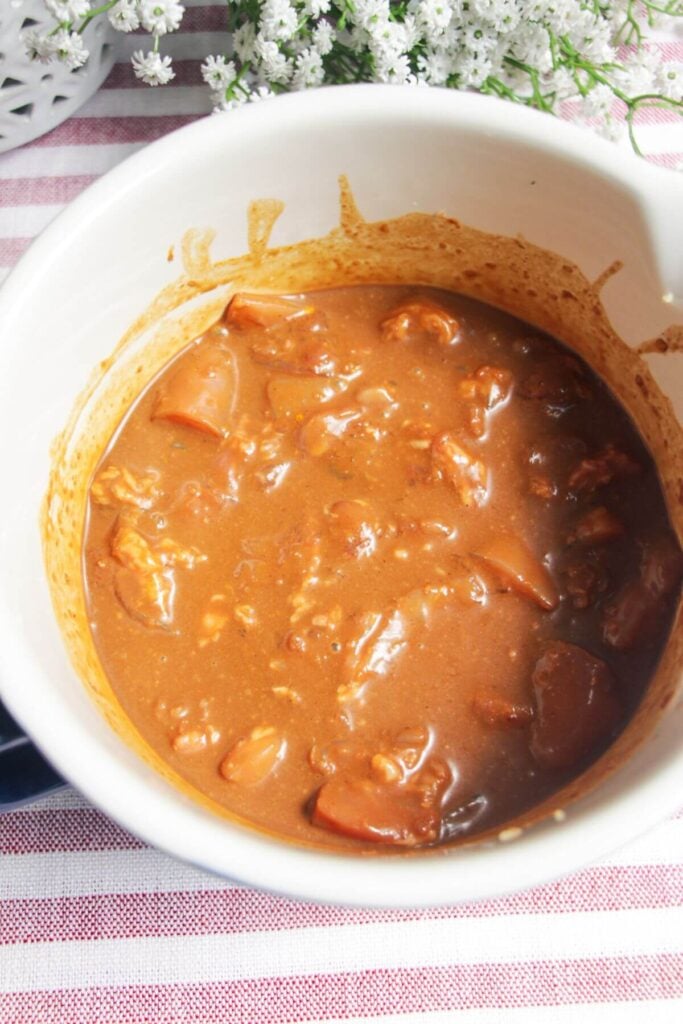 Chicken pieces in a mixing bowl with satay marinade.