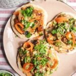 Three chicken satay flatbreads on a pink plate, topped with herbs and peanut sauce.