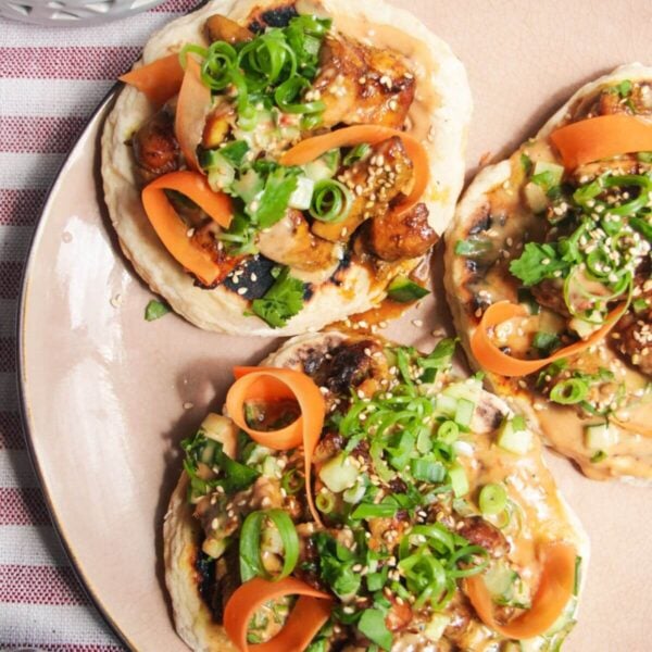 Three chicken satay flatbreads on a pink plate, topped with herbs and peanut sauce.