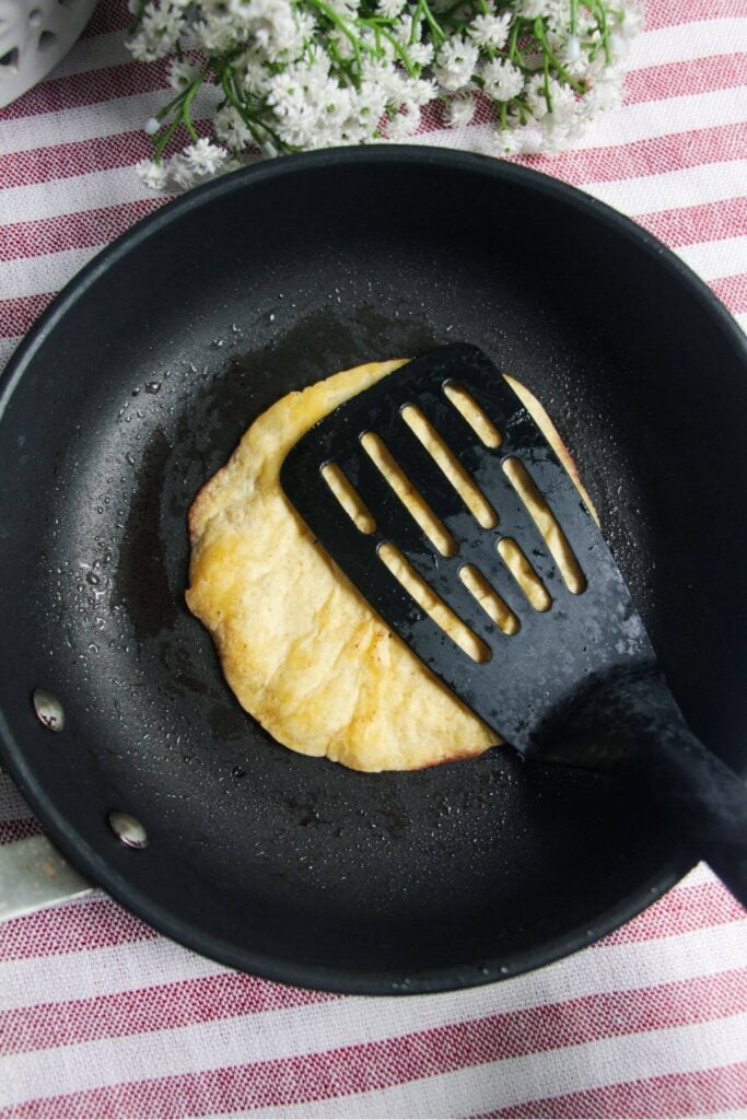 Fish slice pressing mini tortilla into small black pan.
