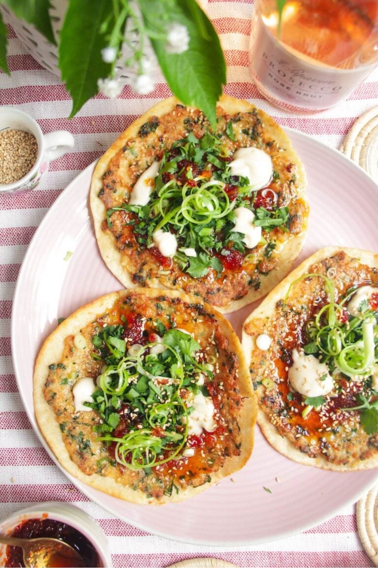 Three prawn toast tacos topped with herbs and aioli on a pink plate.