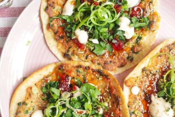 Three prawn toast tacos topped with herbs and aioli on a pink plate.